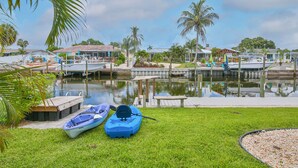 A marina with boats docked, a grassy area with kayaks, and a building with a red roof in the background. - All Docked Out-Bring Your Own Boat! Private Heated Pool, Free WiFi 3 Mins to AMI (Bradenton)