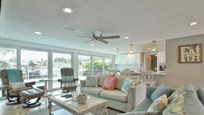 A spacious living room with a large window, a ceiling fan, and a view of the outdoors. - All Docked Out-Bring Your Own Boat! Private Heated Pool, Free WiFi 3 Mins to AMI (Bradenton)