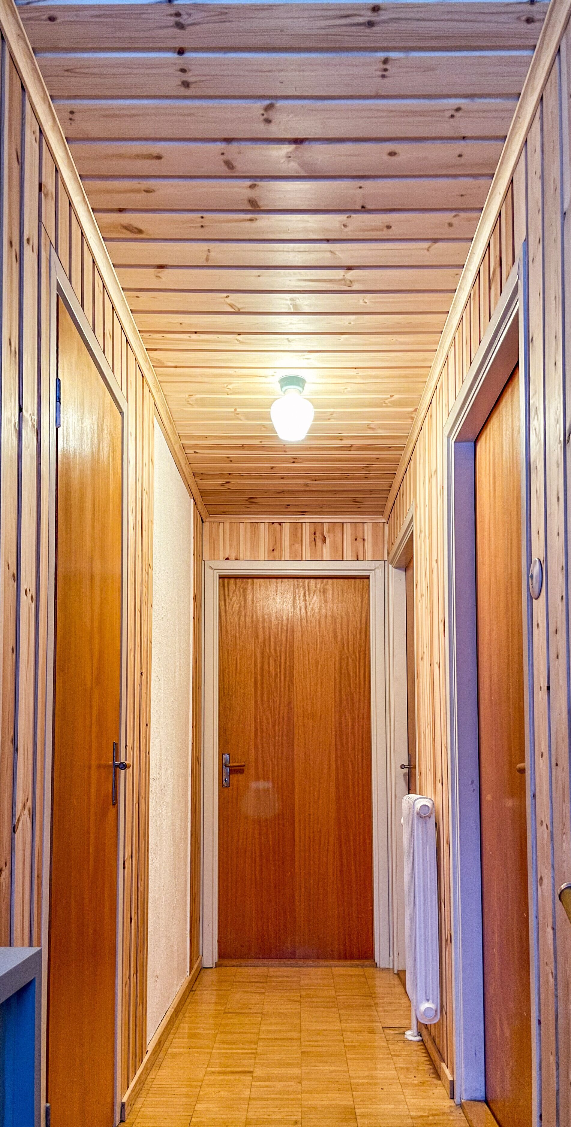 Ein schmaler Korridor mit Holzwänden und einer Holztür am Ende.