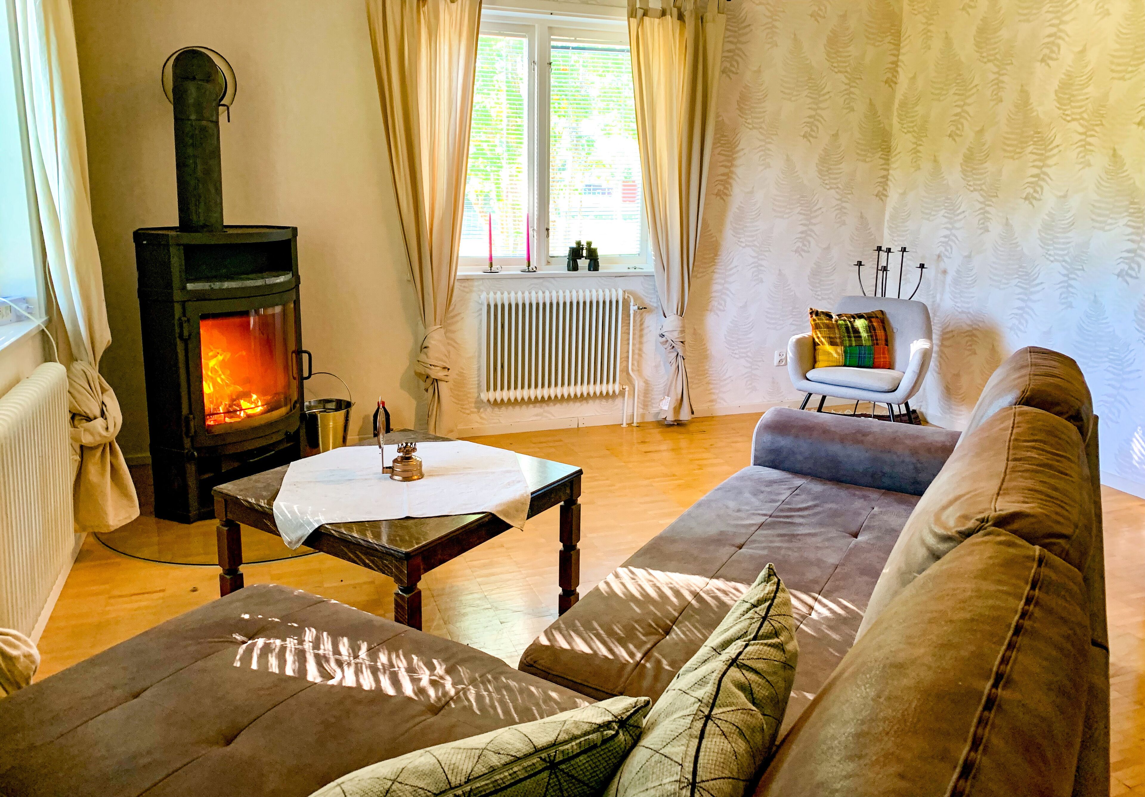 Ein gemütliches Wohnzimmer mit Kaminofen, Sofa, Tisch und Sessel.