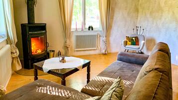 Ein gemütliches Wohnzimmer mit Kaminofen, Sofa, Tisch und Sessel.