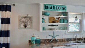 Ett kök med en skylt som visar texten ”BEACH HOUSE”, en köksö formad som en sjöstjärna och ett fönster med utsikt.