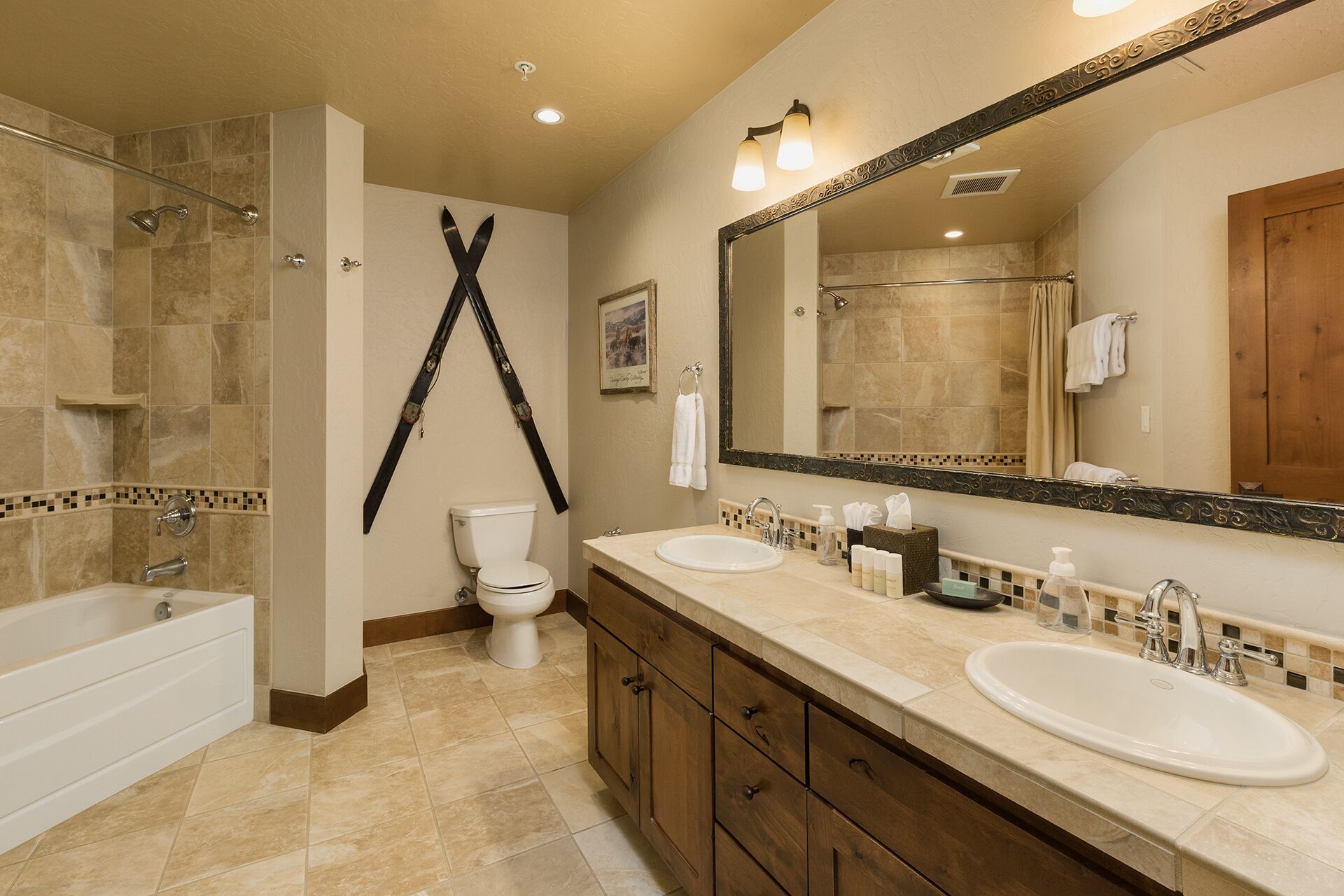 A bathroom with a bathtub, two sinks, a toilet, and a large mirror.