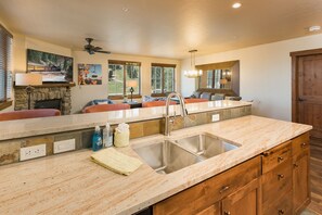 A kitchen with a stone countertop, a stainless steel sink, wooden cabinets, and a ceiling fan. - Premier Building at Purgatory - Ski in/Ski Out - Slopeside Views (Durango)
