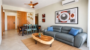 A modern living room with a grey sofa, wooden coffee table, and a dining area with chairs and a wooden partition. - Mar Mary Ocean View (Boca Chica)