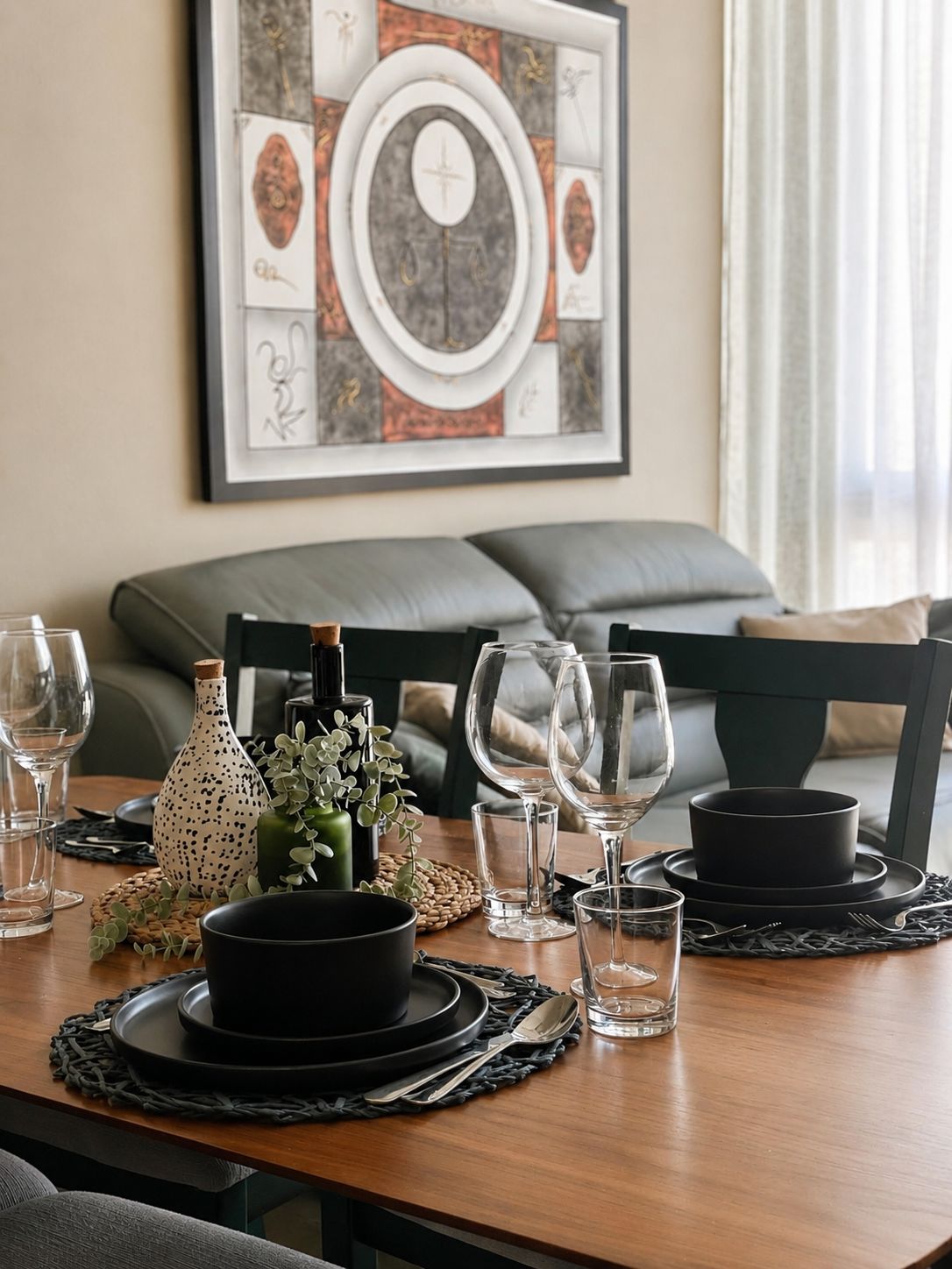 A dining table set with black plates, bowls, and wine glasses, with a decorative vase and greenery on the table.