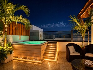 Een terras op het dak met een hottub, houten trappen, een glazen hekwerk en zitplaatsen buiten.