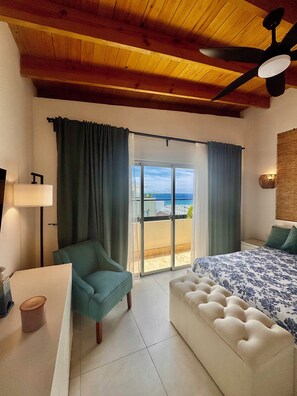 A bedroom with a bed, a chair, a desk, and a view of the beach.