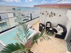 A rooftop terrace with a pool, lounge chairs, and a view of the ocean.