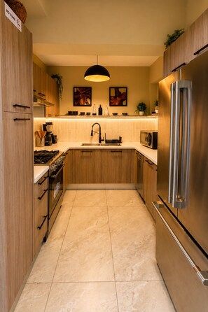 A modern kitchen with wooden cabinets, stainless steel appliances, a central island, and a hanging light fixture. - Mar Mary Ocean View (Boca Chica)