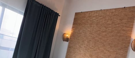Makuuhuoneessa on sänky, kattotuuletin, ikkuna, jossa on verhot, yöpöytä ja seinään kiinnitetty valaisin.