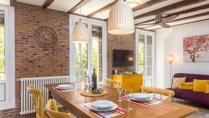 A dining area with a wooden table, yellow chairs, and a brick wall. - Sarriegi | The Rentals Collection (San Sebastián)