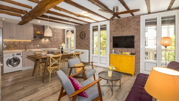 A spacious living area with a kitchen, wooden beams, a TV, and a yellow cabinet. - Sarriegi | The Rentals Collection (San Sebastián)
