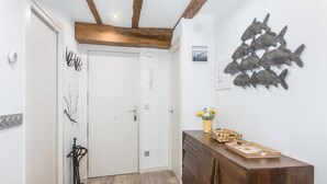 A hallway with a wooden ceiling, a white door, a wall-mounted fish decoration, a wooden cabinet with a tray, and a small plant. - Sarriegi | The Rentals Collection (San Sebastián)