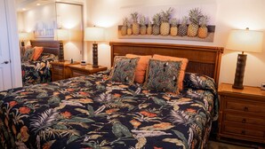 Una habitación de hotel con una cama, dos mesitas de noche, una lámpara, un reloj y un cuadro con piñas en la pared.
