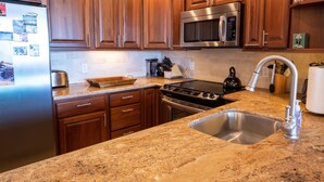 Una cocina con armarios de madera, electrodomésticos de acero inoxidable, encimeras de granito y un lavamanos doble.