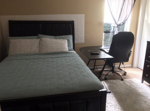 Relax in a spacious room with a large bed, desk, and window with sheer curtains.