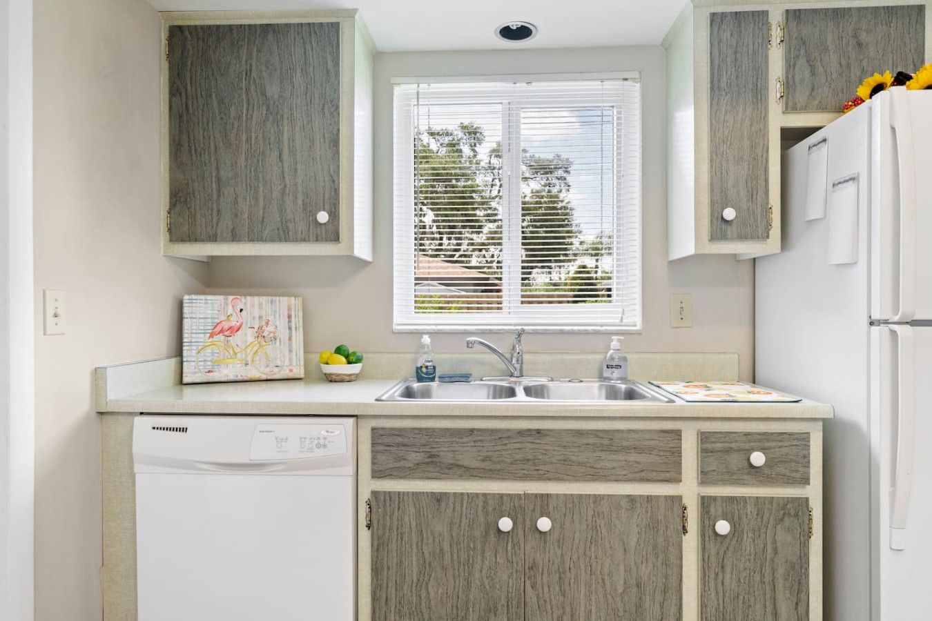 A kitchen with wooden cabinets, a dishwasher, a sink, and a window with blinds.
