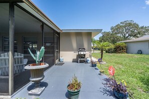 Ein modernes Haus mit überdachter Terrasse, Grill und verschiedenen Topfpflanzen.