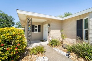 A house with a covered porch, a door, and a small garden with various plants and a pathway. - Cottage w/lanai and garage, 4 mi. Siesta Key (Sarasota)