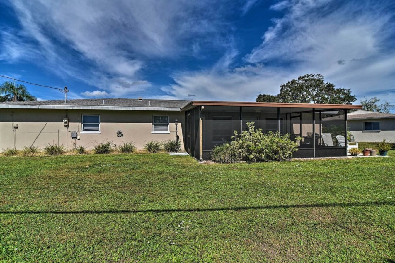 A single-story house with a covered patio area, a lawn, and a clear sky.