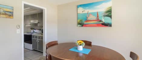 A dining area with a wooden table, four chairs, and a painting of a pier.
