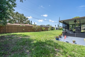 A backyard with a wooden fence, a patio with outdoor furniture, and a house with a glass facade. - Cottage w/lanai and garage, 4 mi. Siesta Key (Sarasota)