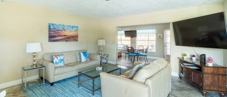 A living room with a beige sofa, a glass coffee table, a blue striped rug, a flat-screen TV, and a wooden entertainment center.