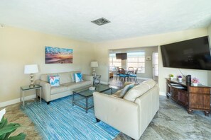 A living room with a beige sofa, a glass coffee table, a blue striped rug, a flat-screen TV, and a wooden entertainment center. - Cottage w/lanai and garage, 4 mi. Siesta Key (Sarasota)