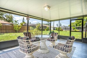 A covered patio with wicker furniture and a glass table, overlooking a backyard with a wooden fence and greenery. - Cottage w/lanai and garage, 4 mi. Siesta Key (Sarasota)