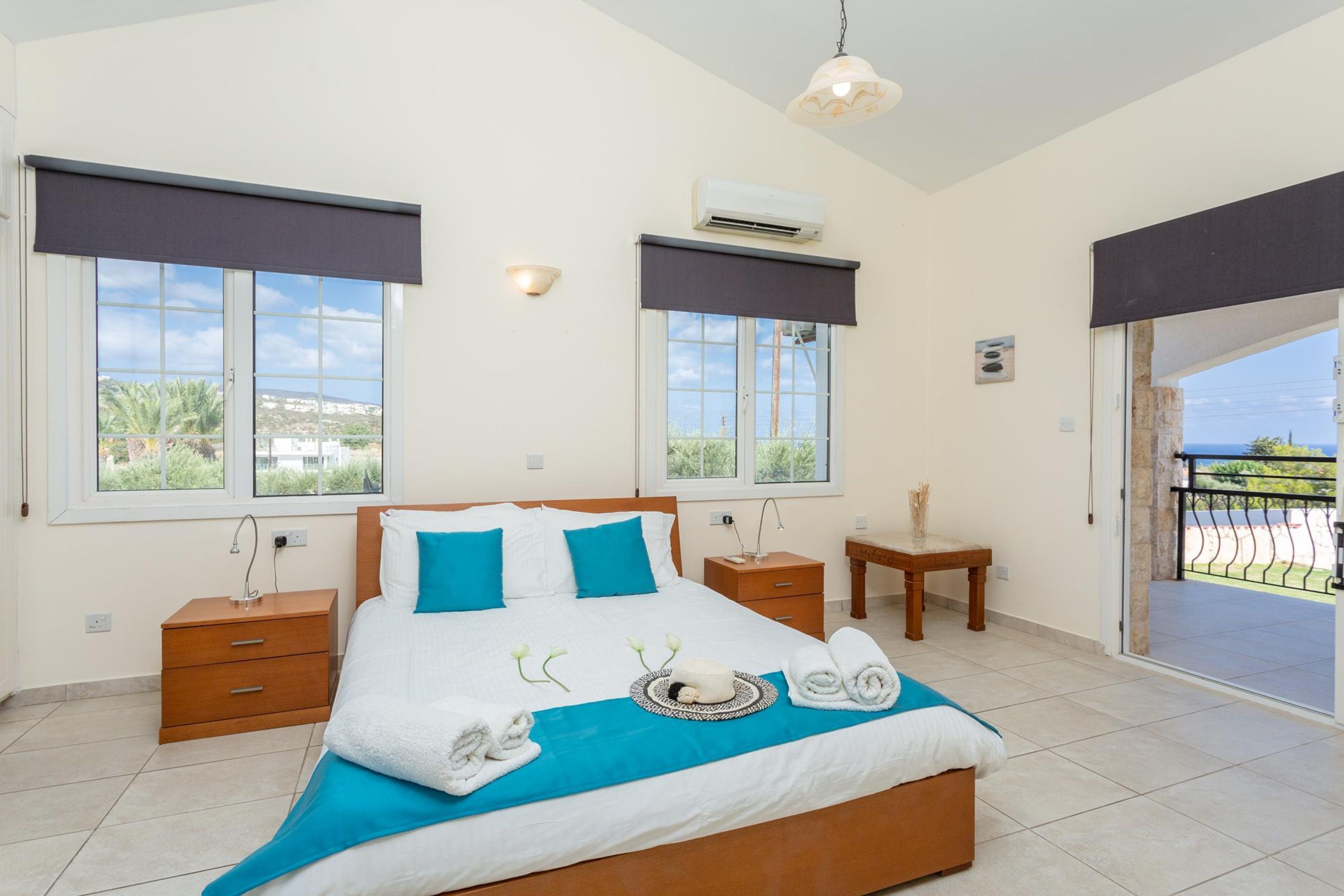 A bedroom with a bed, two bedside tables, a nightstand, a window with a view, and an air conditioning unit.