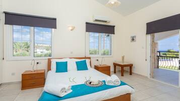 A bedroom with a bed, two bedside tables, a nightstand, a window with a view, and an air conditioning unit.