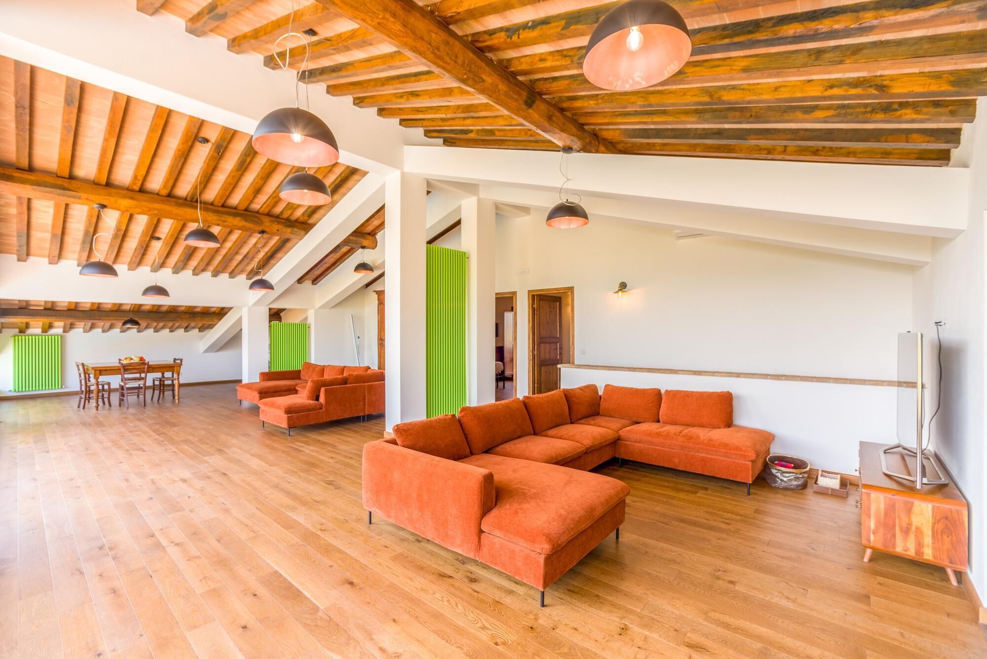 Un'ampia zona giorno con parquet, un grande divano modulare arancione e un tavolo da pranzo con sedie.