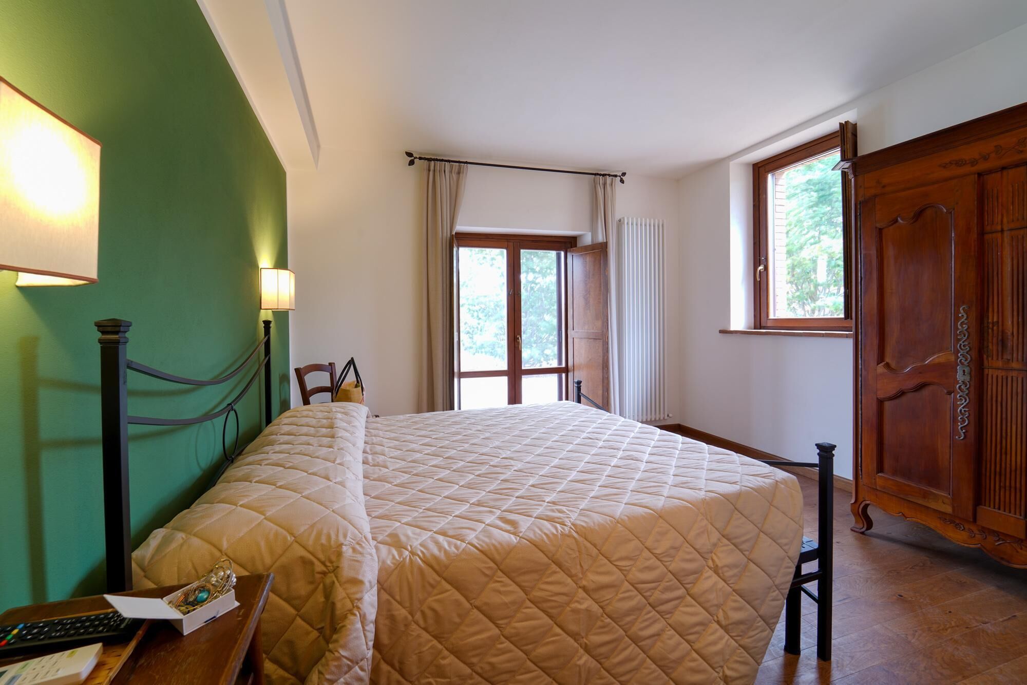 A bedroom with a bed, a desk with a keyboard, a lamp, a window with curtains, and a wooden wardrobe.