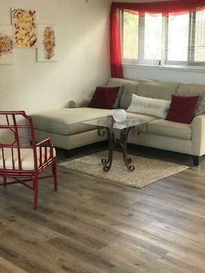 Un salon avec un canapé beige, des coussins rouges à motifs, une table basse en verre et un fauteuil rouge.