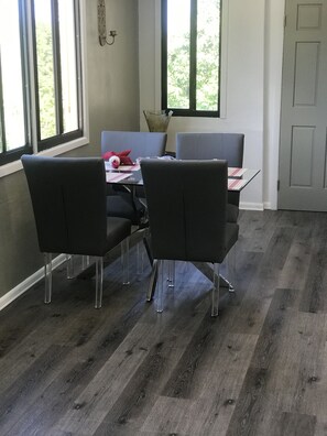 Un coin repas avec une table dressée pour quatre personnes, quatre chaises et une fenêtre donnant sur un paysage verdoyant.