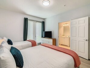Et hotelværelse med to senge, et fjernsyn, et badeværelse med spejl og lys samt en dør.