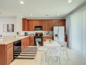Una cocina moderna con armarios de madera, una isla central y un comedor con sillas blancas.