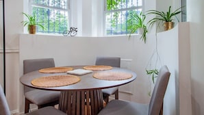 A dining area with a round table, grey chairs, and woven placemats. There are two windows with plants on the windowsill and a bicycle decoration on the wall. - Fancy 1-BR in Central Location (Washington)