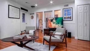 A modern living room with a flat-screen TV, wooden flooring, and a large window. - Fancy 1-BR in Central Location (Washington)