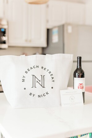 A kitchen counter with a white bag labeled "My Beach Retreat by Nick," a bottle of wine, and a small card.