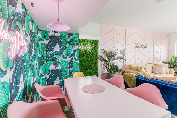 A modern dining area with a white table, pink chairs, and a neon sign.