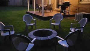 Un patio aménagé dans le jardin, avec un foyer, des chaises et un espace repas couvert.