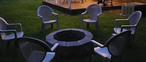 Un patio trasero con un brasero, sillas y un comedor techado.