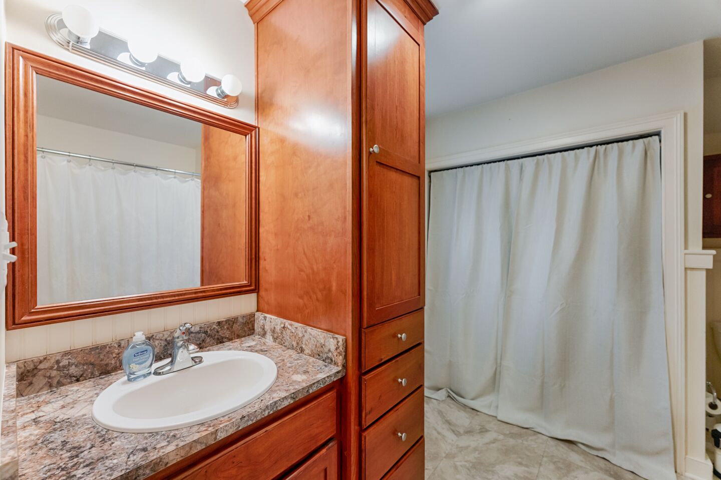 A bathroom with a wooden vanity, a large mirror, a sink, and a shower curtain.