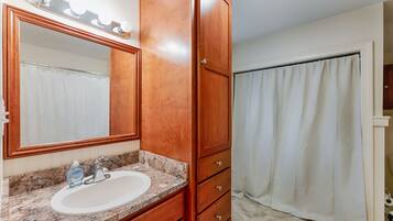 A bathroom with a wooden vanity, a large mirror, a sink, and a shower curtain.