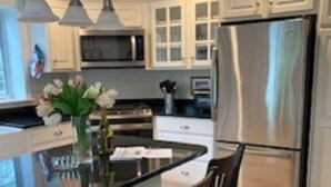 Una cocina moderna con una isla central, sillas de madera oscura, armarios blancos y electrodomésticos de acero inoxidable.