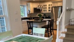 Un comedor con mantel verde, sillas blancas y suelo de madera.