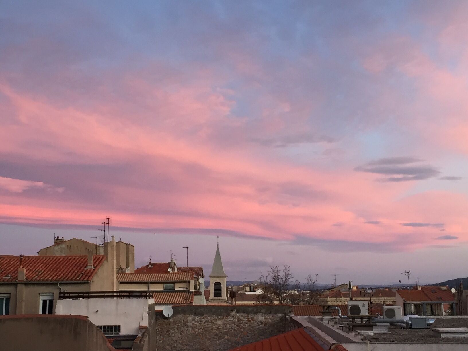 A cityscape with a church steeple and residential buildings under a pink and blue sky.