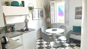 A modern kitchen with a checkered floor, a dining area with a round table and chairs, and a window with a view of the street.